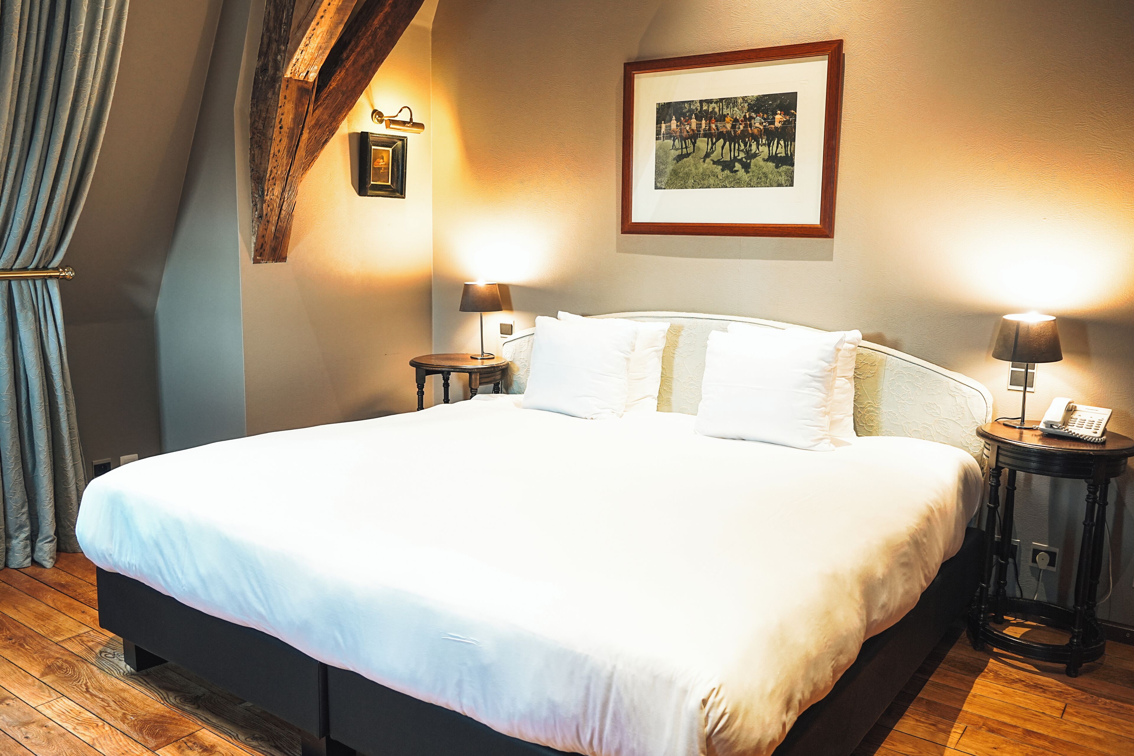 Un lit bien fait dans une chambre d’hôtel, avec un plancher en bois, deux tables de chevet avec des lampes et un tableau encadré au mur.