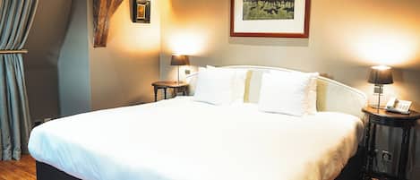 A neatly made bed in a hotel room with a wooden floor, two bedside tables with lamps, and a framed picture on the wall.