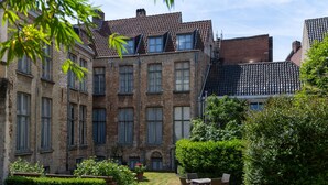 Un patio con un edificio de ladrillo, un pequeño jardín y mobiliario exterior.