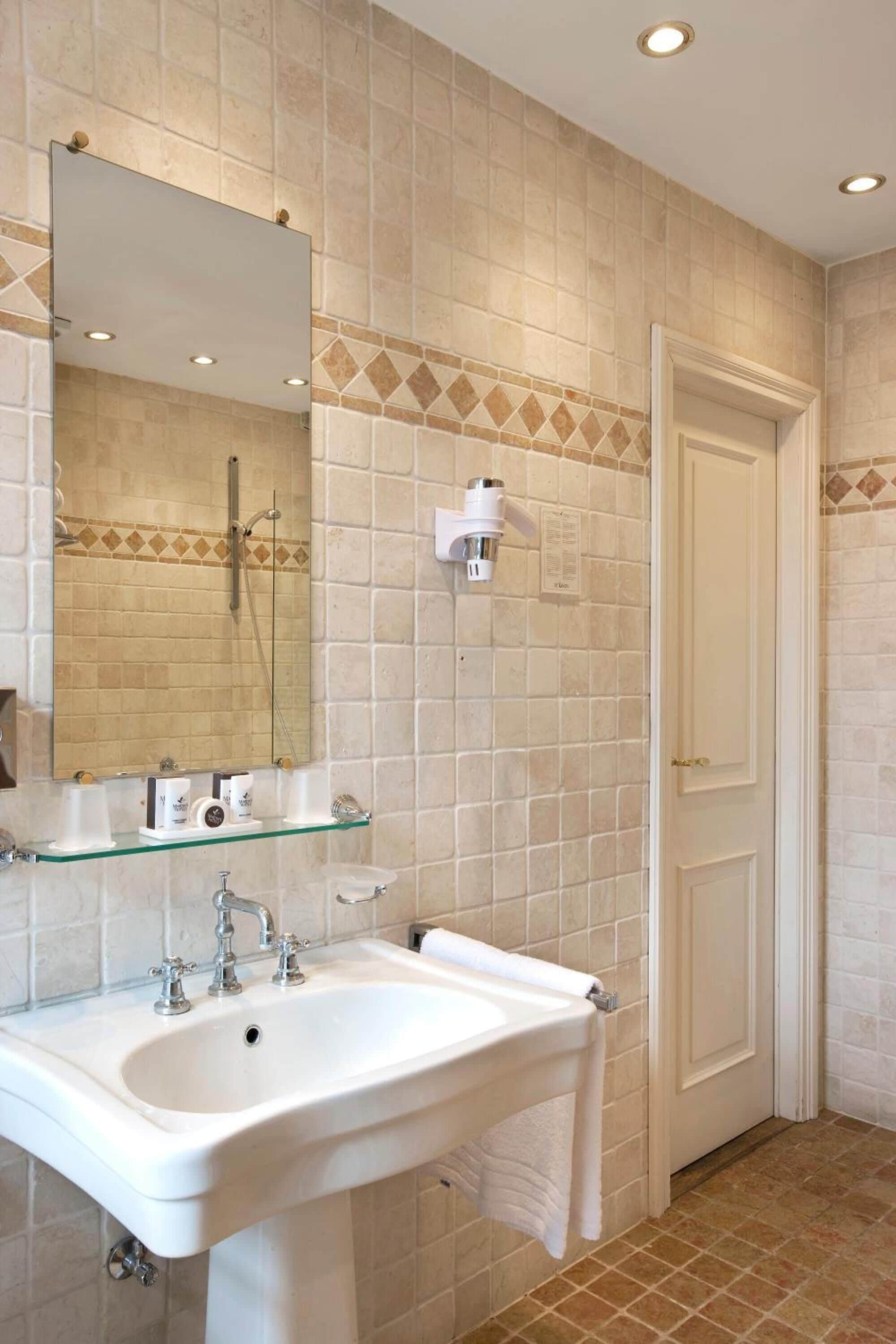 A bathroom with a white sink, a glass shelf, a mirror, and a shower.