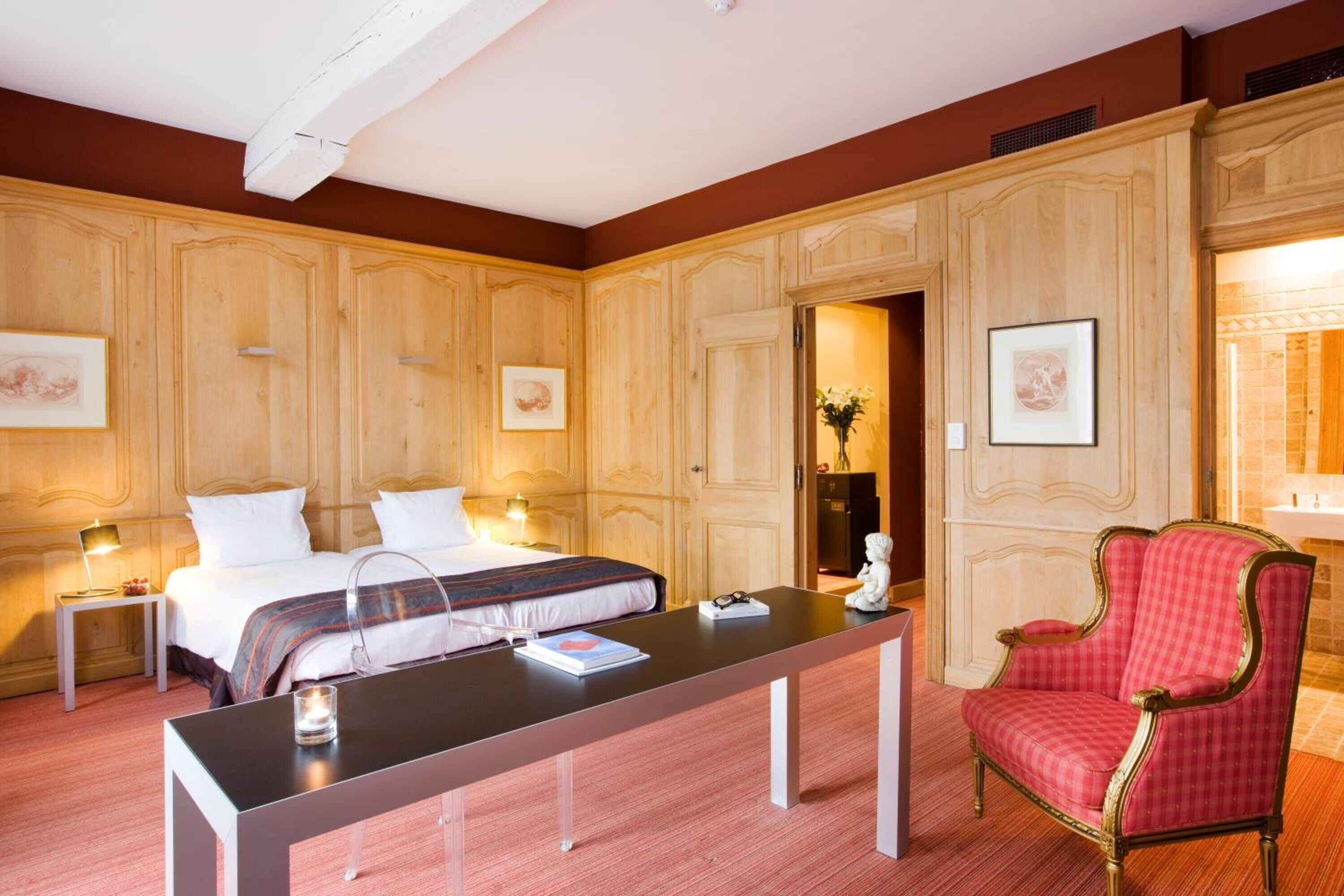 A hotel room with a large bed, a desk, a chair, and wooden paneling on the walls.