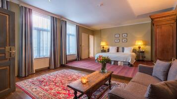 A hotel room with a large bed, a sitting area with a sofa and a coffee table, a red patterned rug, and a wooden cabinet.