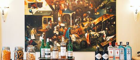 Una zona de bar con un cuadro grande, diversas botellas de licor y frascos de nueces sobre la barra.