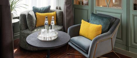 A room with a grey armchair, a round table with a tray of glasses, and a green cabinet with glass doors.