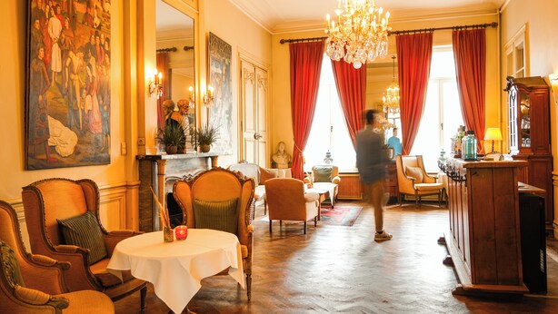 Un vestíbulo de hotel con un cuadro grande, una araña y una zona de comedor con mesas y sillas.