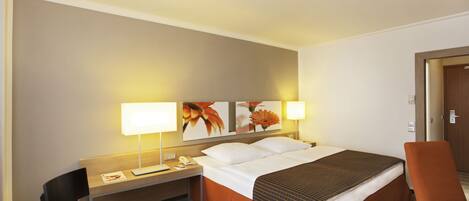 A hotel room with a bed, a desk, a chair, and a nightstand.