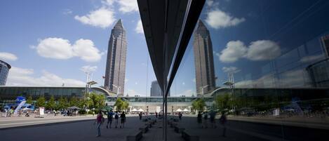A modern urban plaza with two tall buildings, a glass structure, and a clear blue sky.