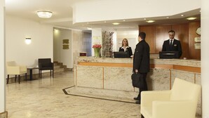 Ein Hotel-Empfangsbereich mit einer Marmor-Rezeption, einer Wartezone mit Sitzgelegenheiten und einer Treppe, die zu einer anderen Etage führt.