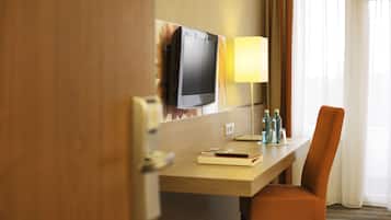 Habitación de hotel con un escritorio de madera, una silla, televisor montado en la pared, lámpara y ventana con cortinas.