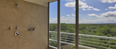 A bathroom with a large window, a shower, and a view of greenery.
