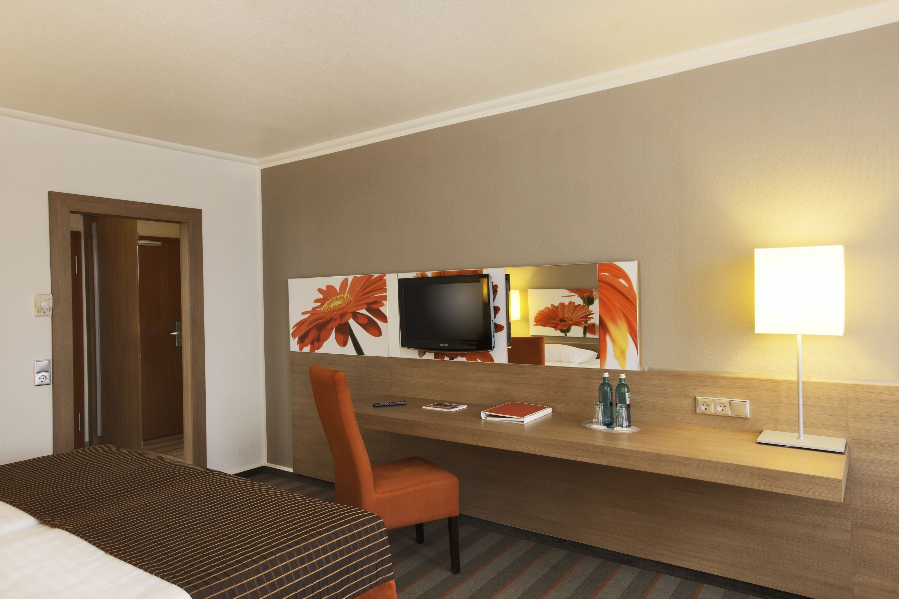 A hotel room with a bed, a desk with a chair, a television, and a lamp.