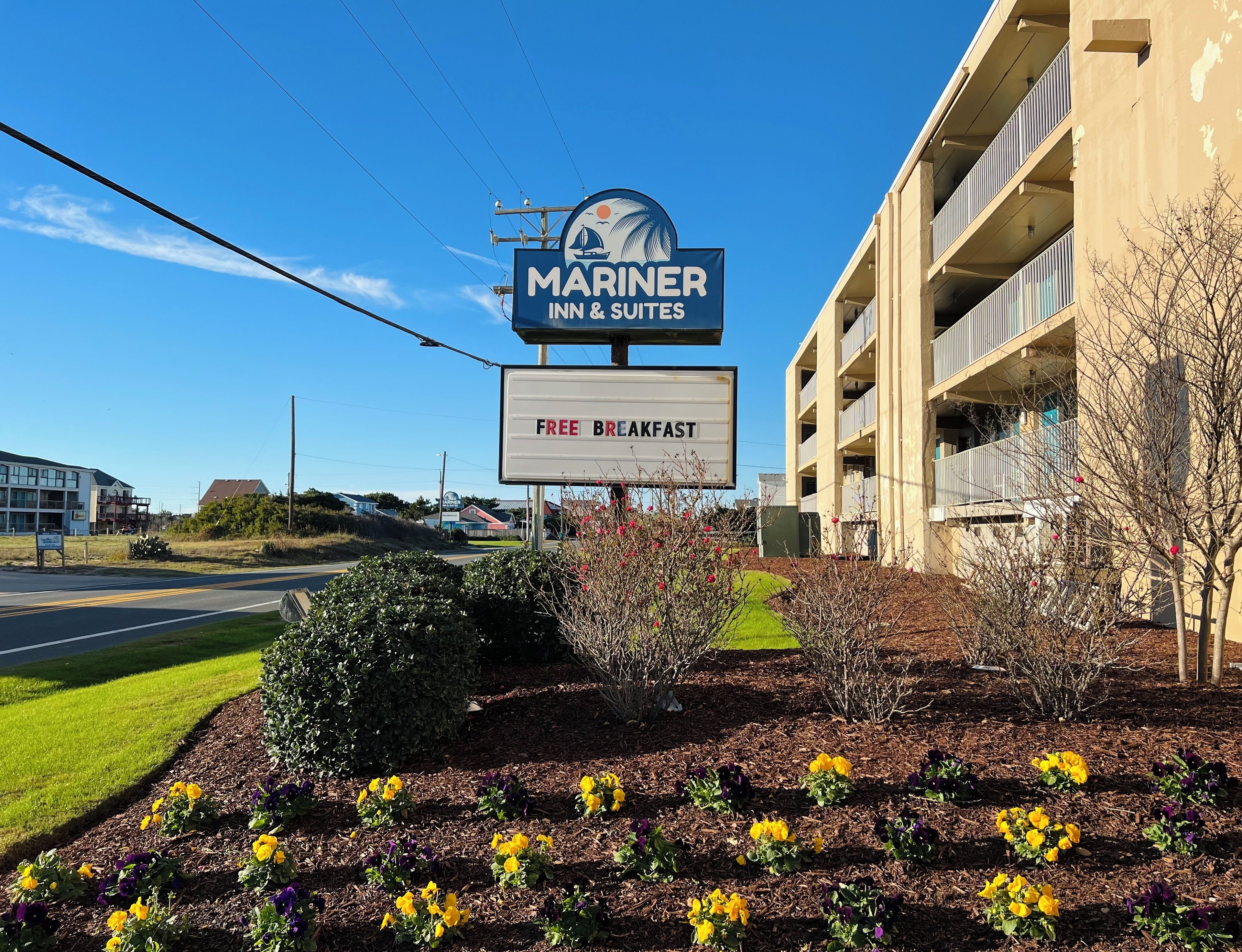 A Mariner Inn & Suites sign with a free breakfast offer, surrounded by a landscaped garden with flowers.