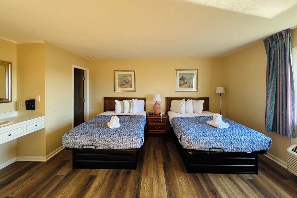 A hotel room with two beds, wooden flooring, a dresser, and a door.