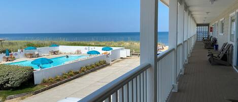 A covered outdoor area with a pool, lounge chairs, and a view of the beach and ocean.