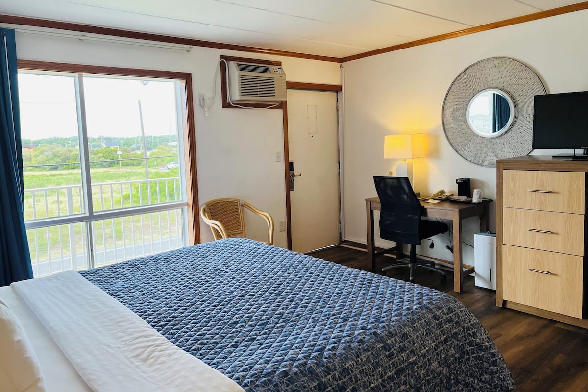 A hotel room with a bed, a desk with a chair, a TV, a lamp, and a wardrobe.