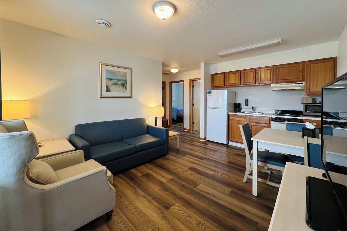 A modern living room with a sofa, a dining table, and a kitchen area with wooden cabinets and appliances.