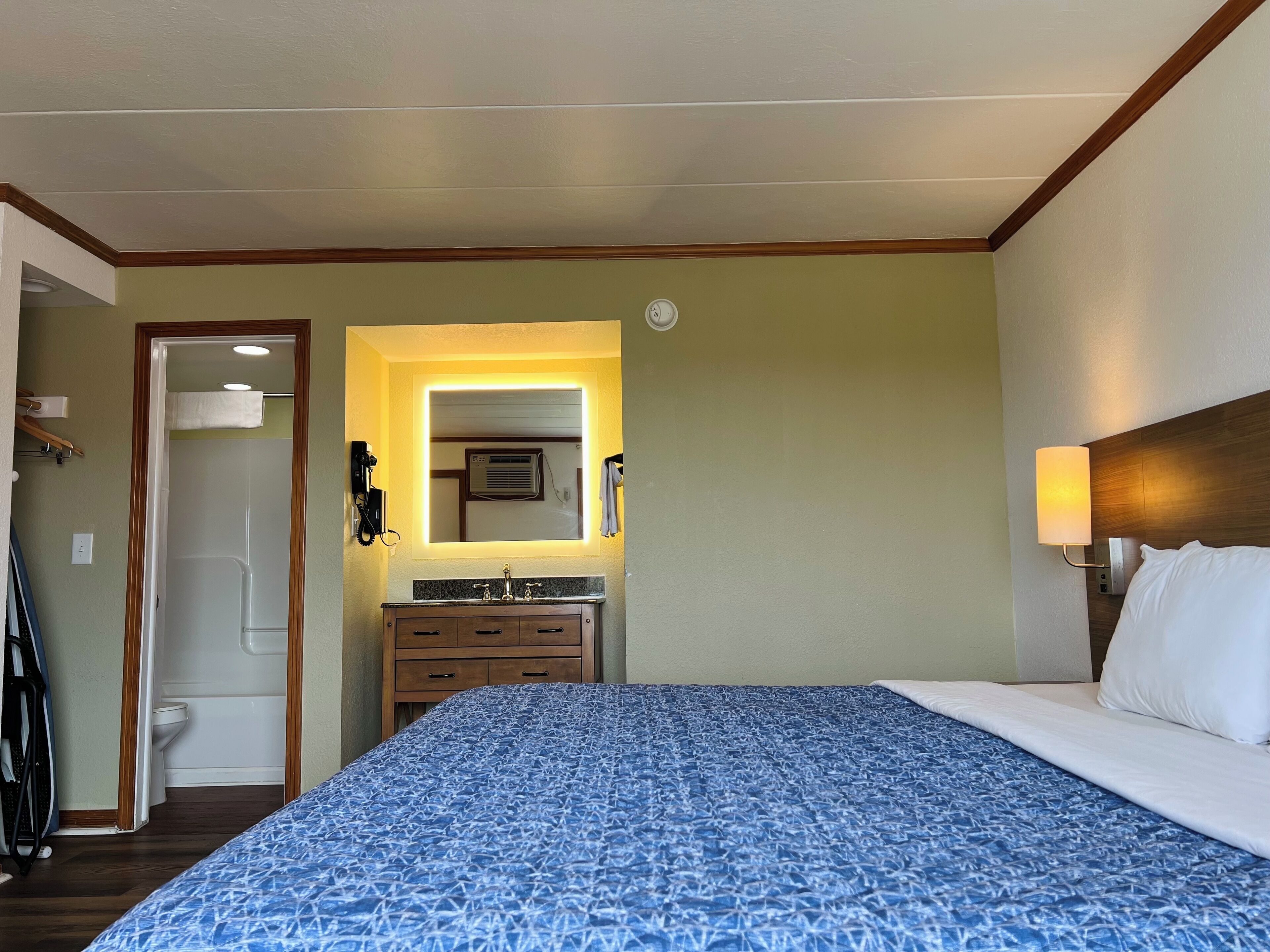 Ein Hotelzimmer mit einem Bett, einem Badezimmer mit Waschbecken und Spiegel sowie einem Holzkopfteil.