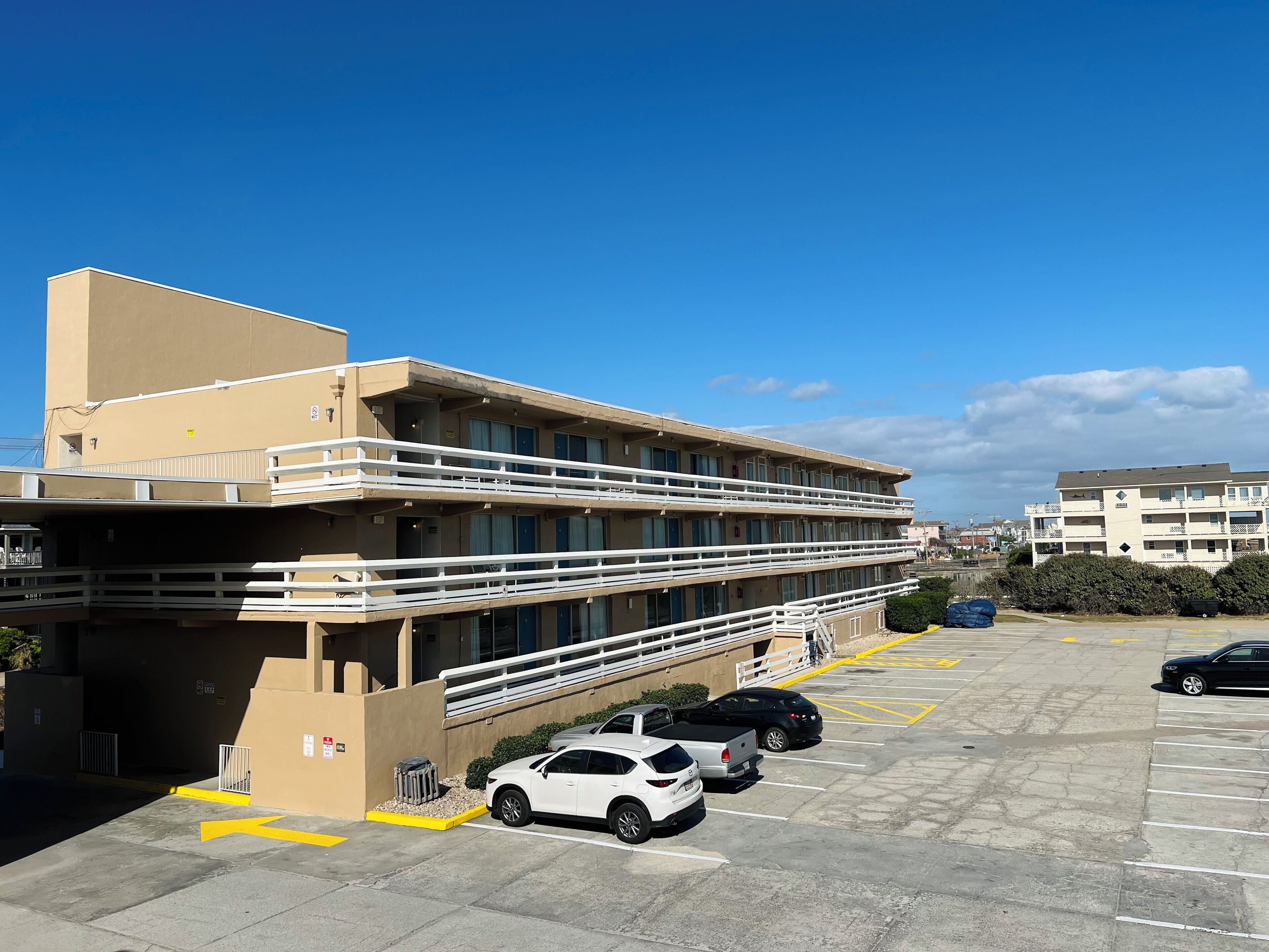 A multi-story hotel with balconies, a parking lot, and a clear blue sky.