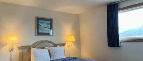 A hotel room with a bed, two bedside lamps, a painting on the wall, and a window with curtains.