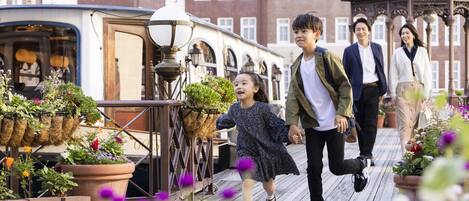 Una familia caminando sobre una terraza de madera con plantas y flores en macetas.
