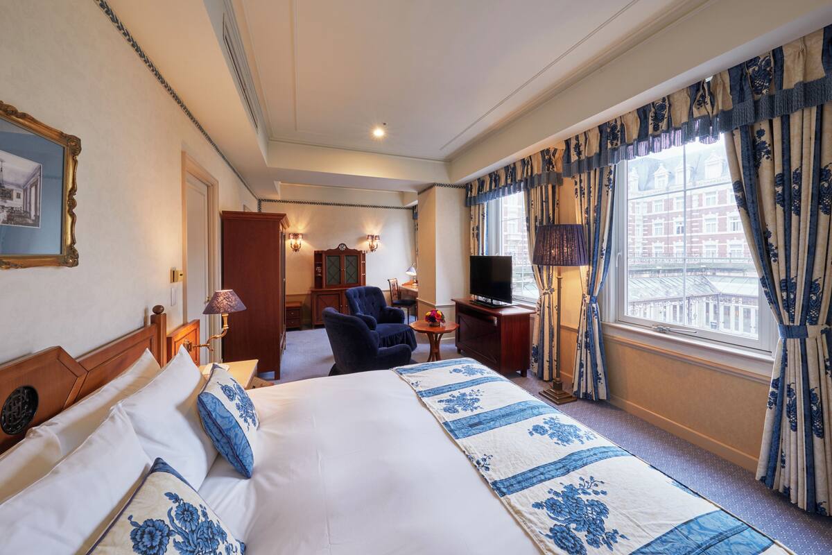 A hotel room with a bed, a chair, a television, and a window with curtains.