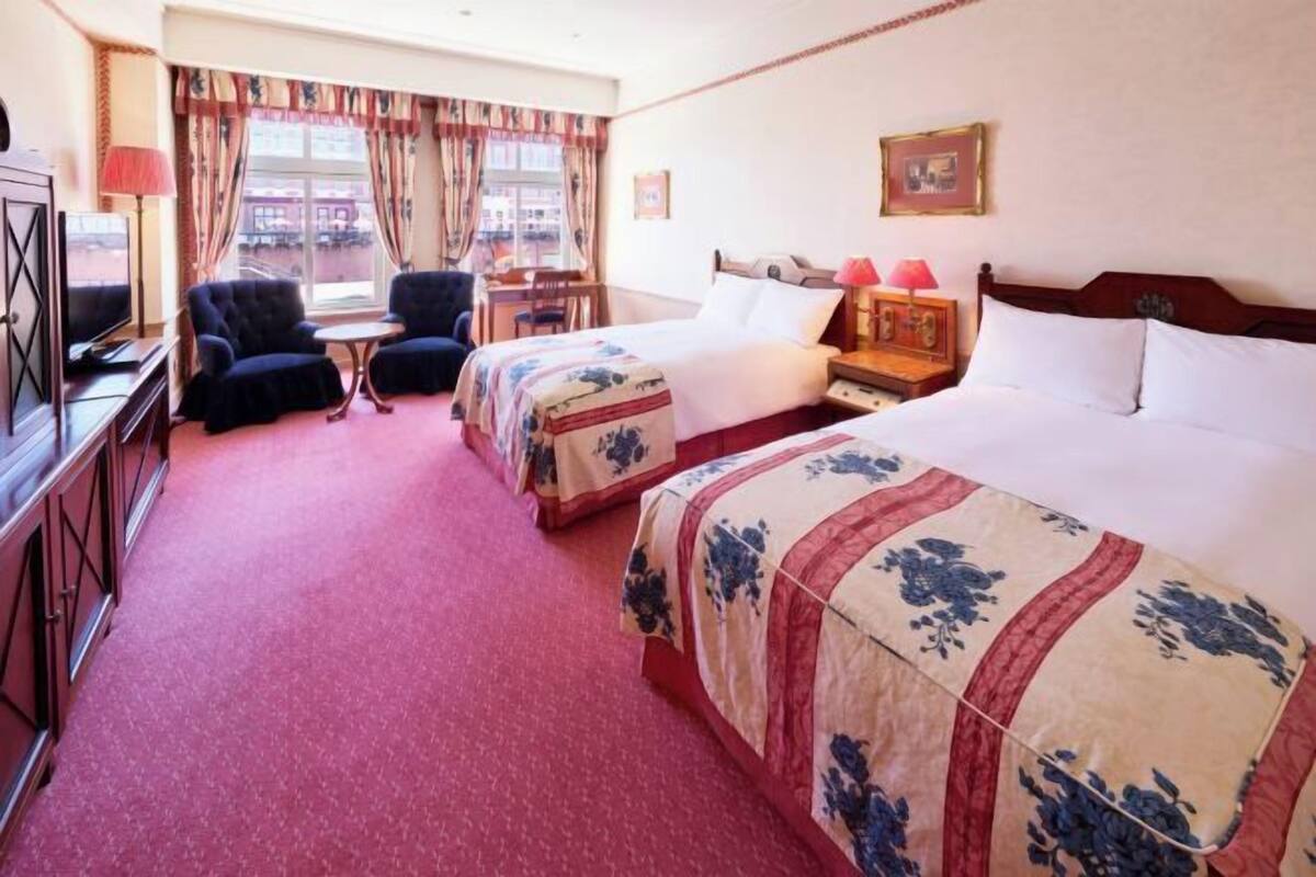 A hotel room with two beds, a desk, a chair, a television, and a window with curtains.