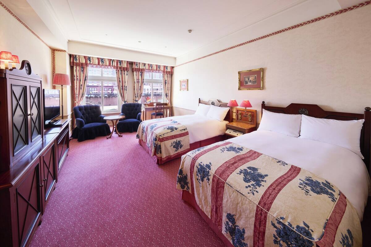 A hotel room with two beds, a desk, a chair, a television, and a window with curtains.
