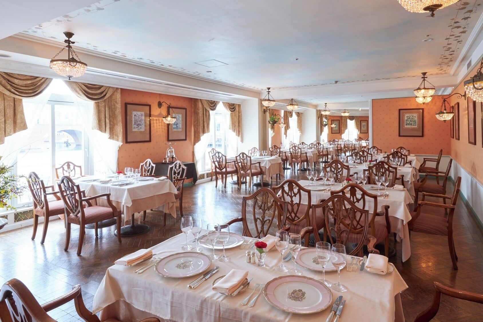 A formal dining room with multiple tables, chairs, and chandeliers.