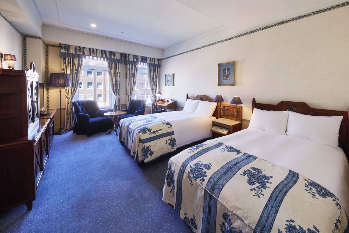 A hotel room with two beds, a desk, a chair, and a wardrobe.