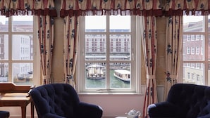 A room with two dark blue armchairs, a wooden table with a teapot and cups, and a view of a canal with buildings and a bridge. - Hotel Europe Huis Ten Bosch (Sasebo)