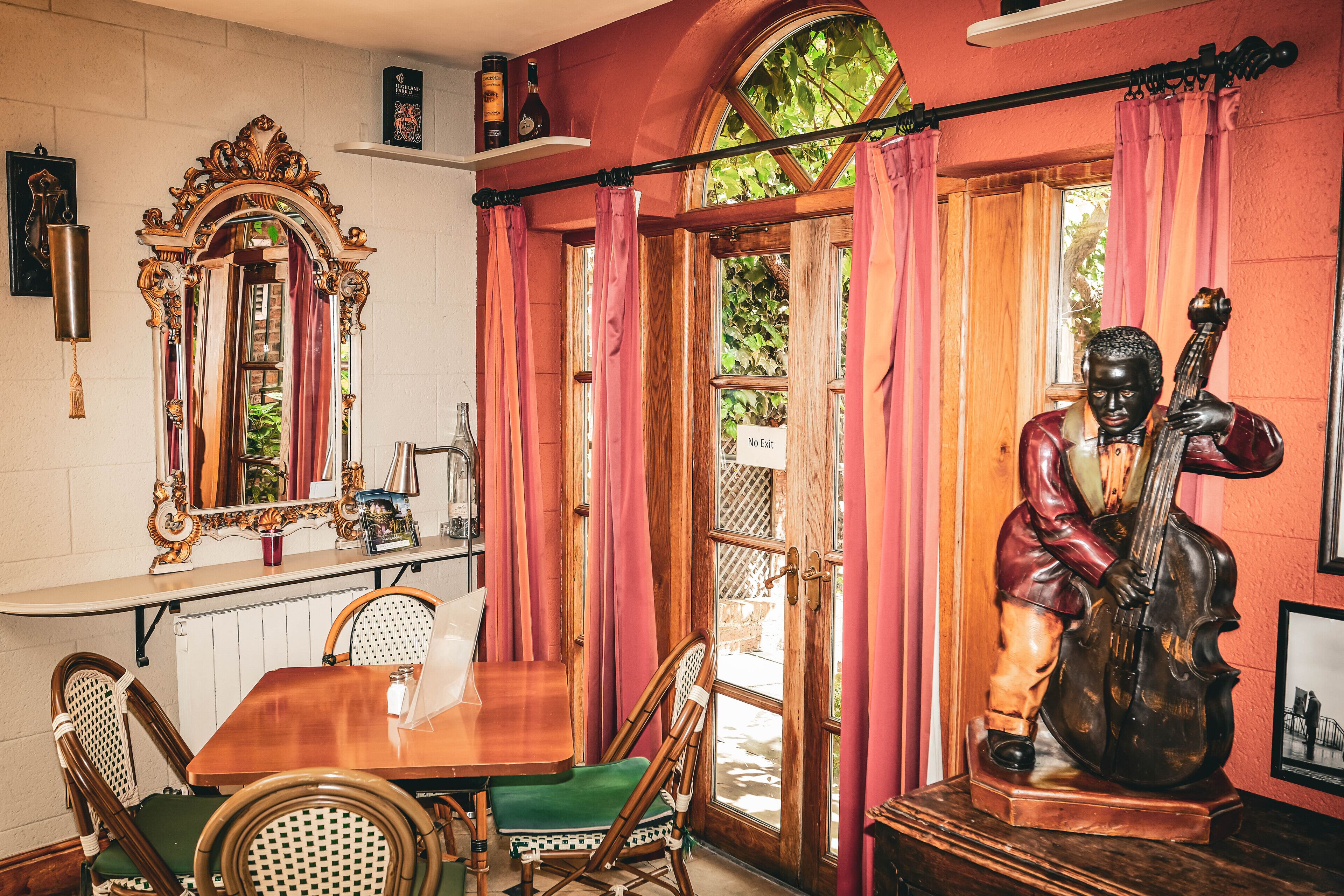 A dining area with a wooden table, wicker chairs, a mirror, and a statue of a musician.