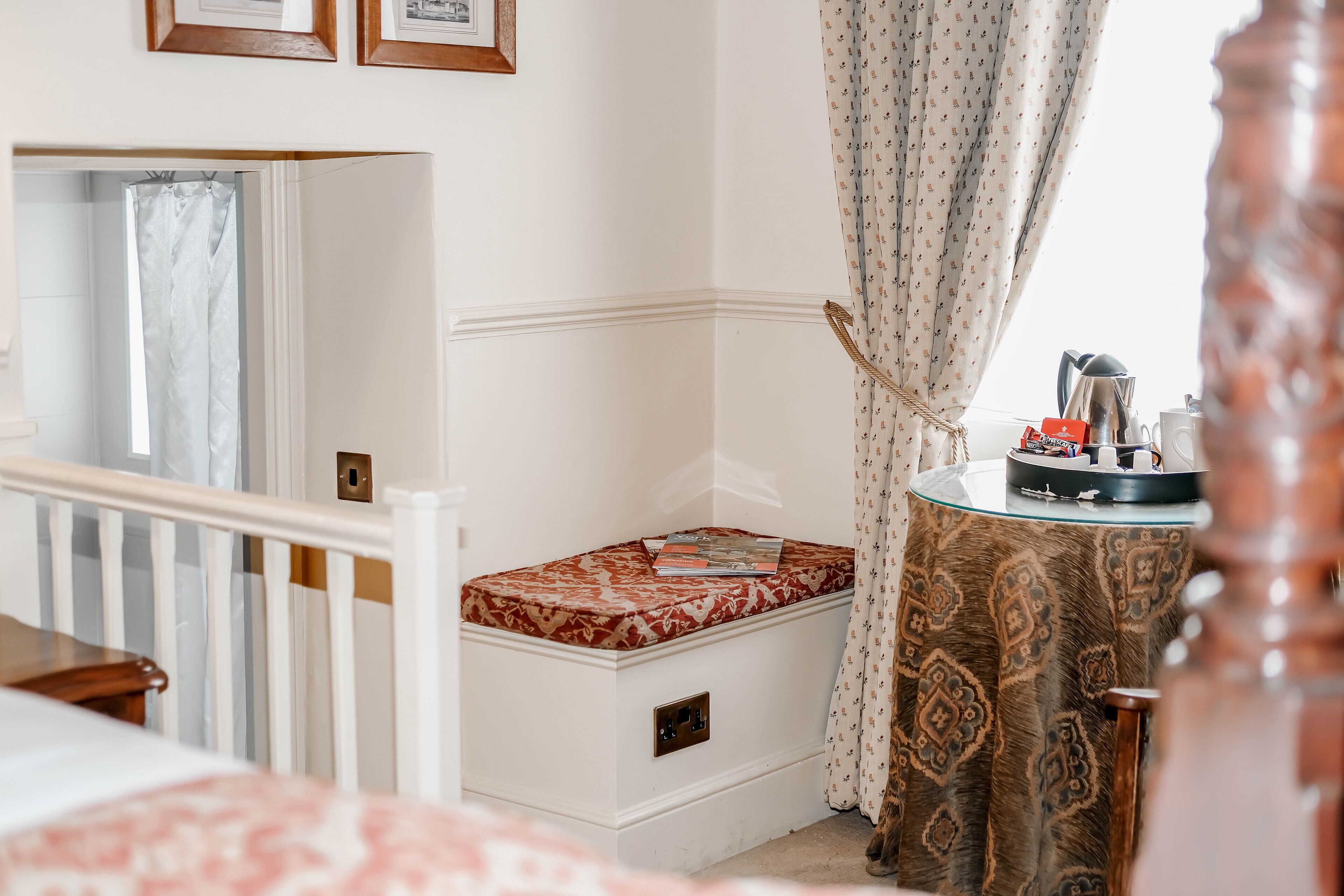 Une pièce avec un berceau blanc, une petite table recouverte d’une nappe à motifs et un miroir accroché au mur.
