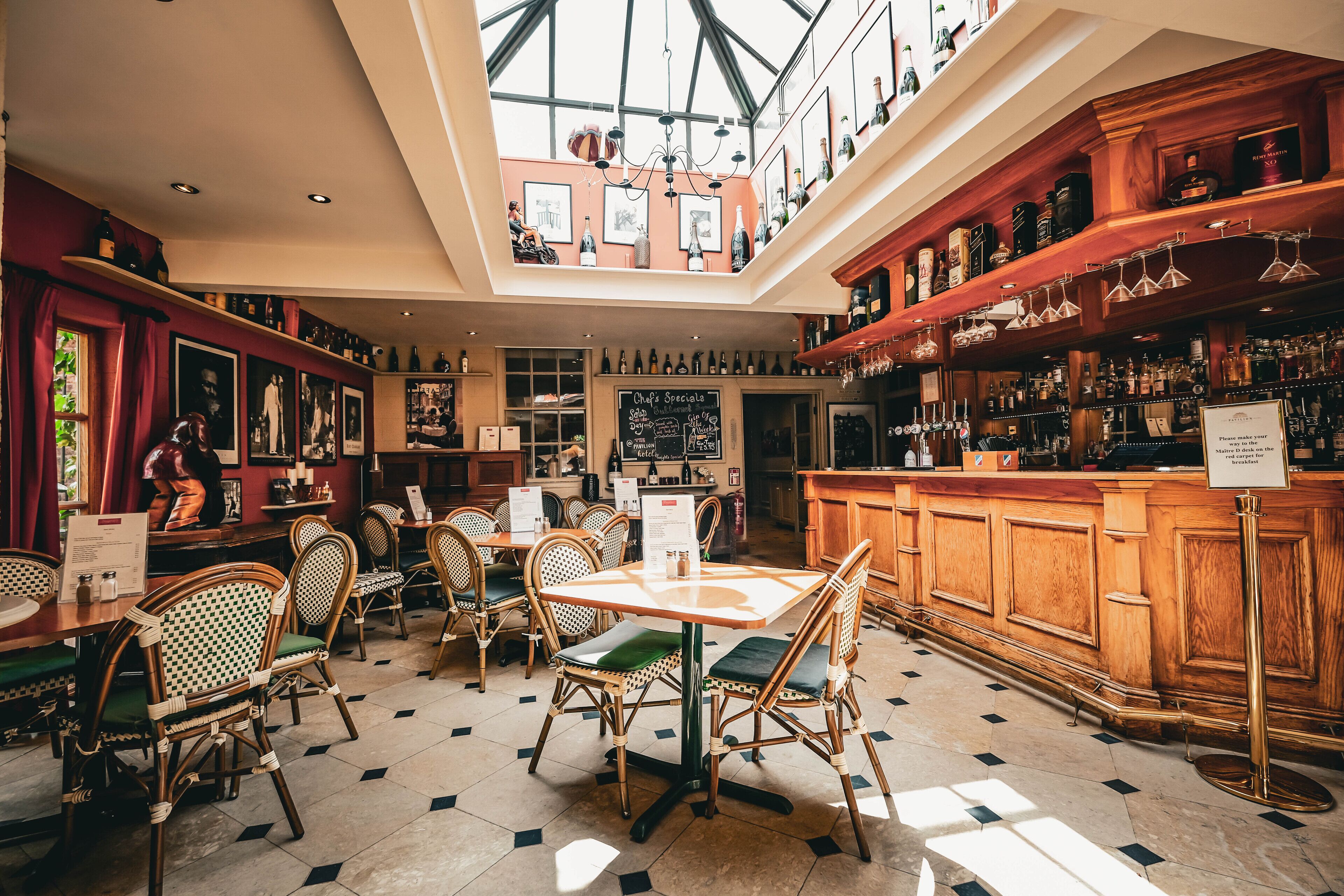 A restaurant with a high ceiling, wooden bar, and wicker chairs.