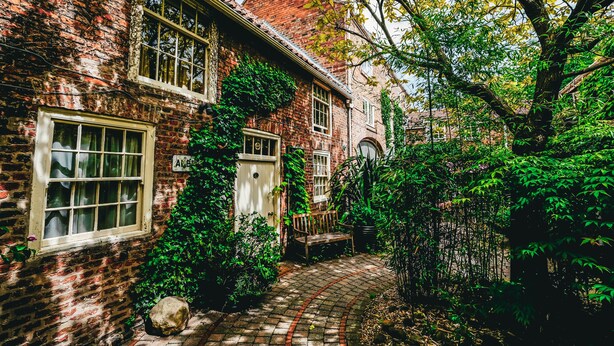 Ein Ziegelhaus mit Gartenweg, Bank und einem großen Baum.