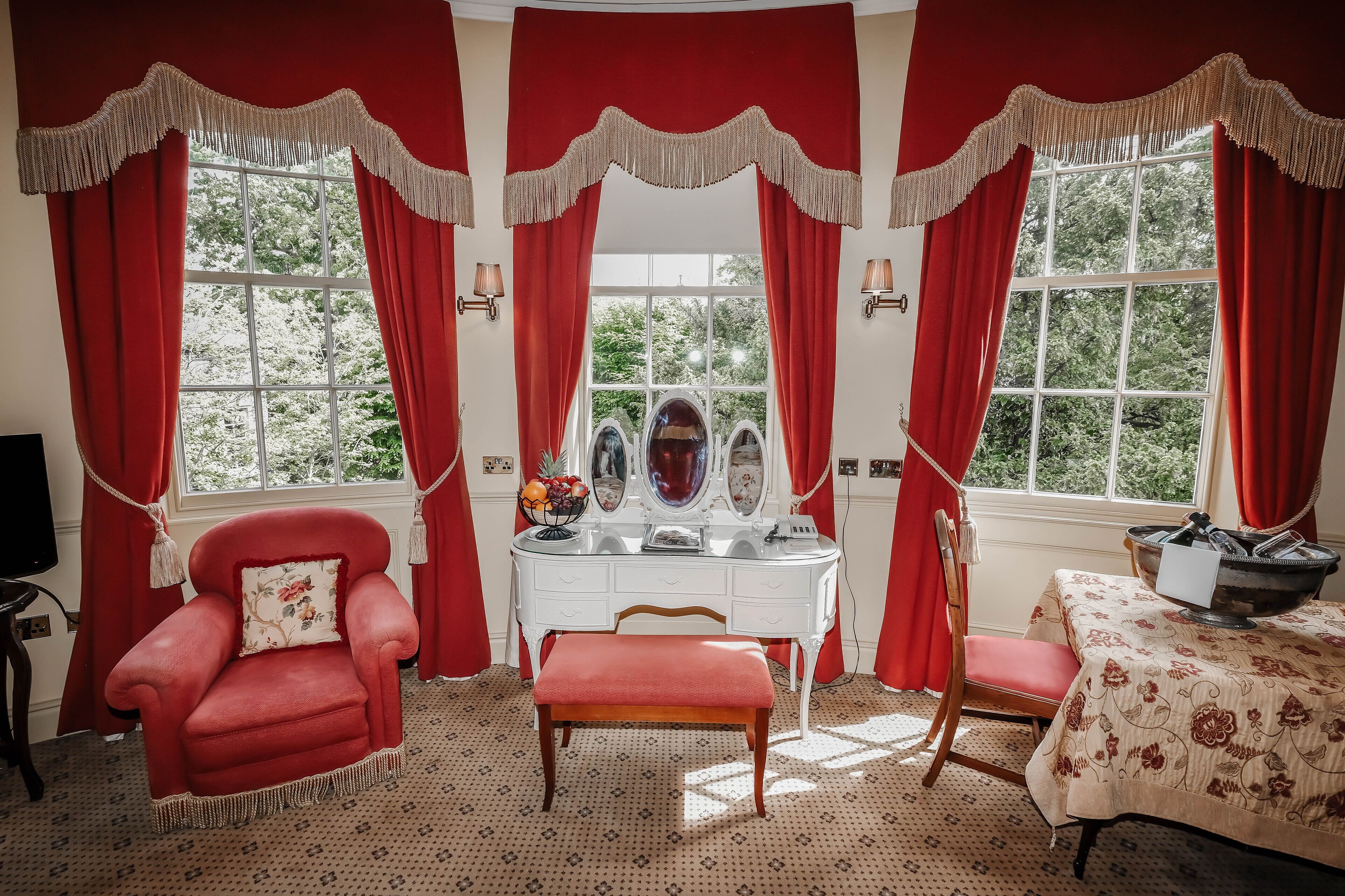 A room with a red armchair, a vanity with a mirror, and a table with a floral tablecloth.