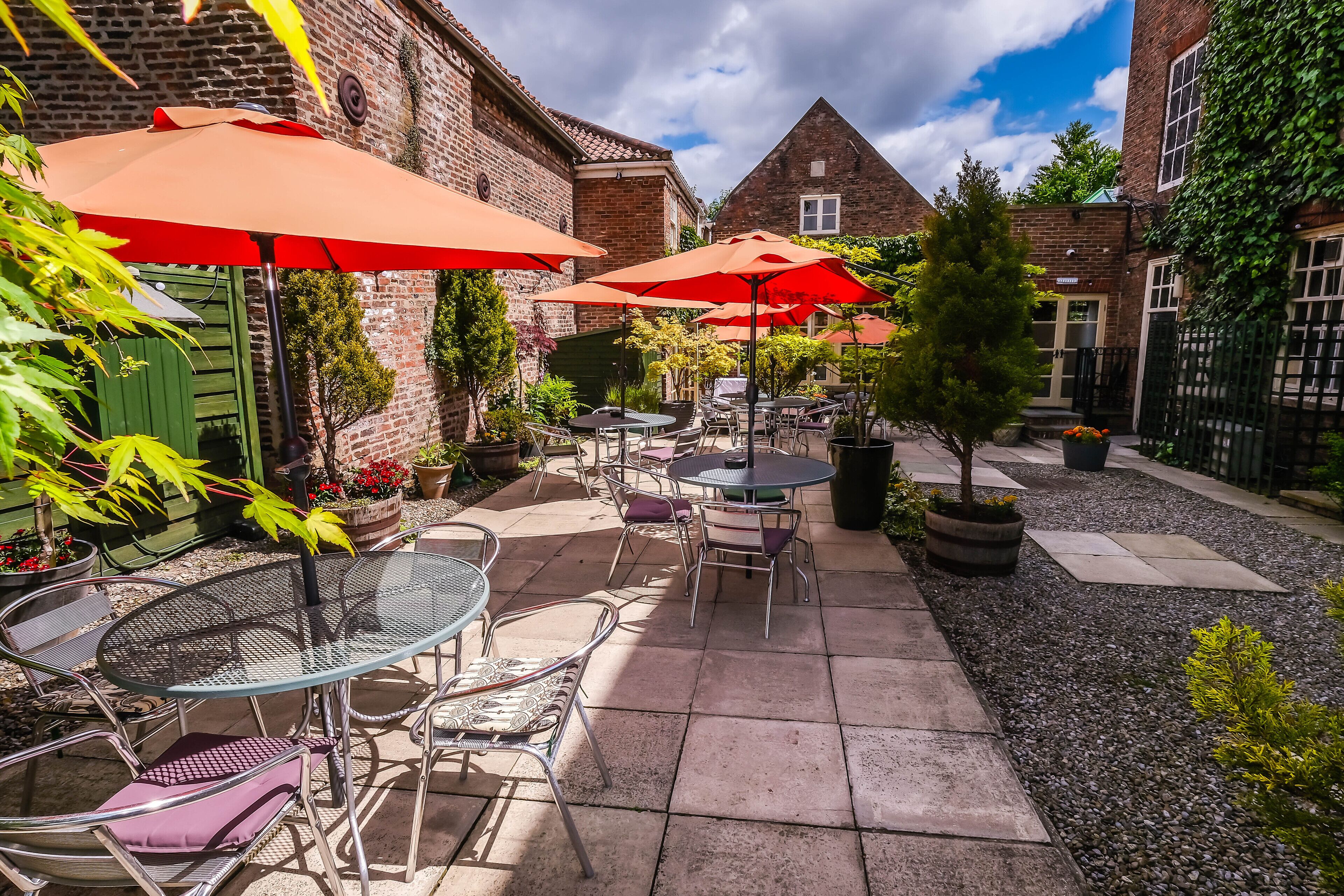 Une cour avec des espaces de repos en plein air, des parasols rouges et des bâtiments en briques.