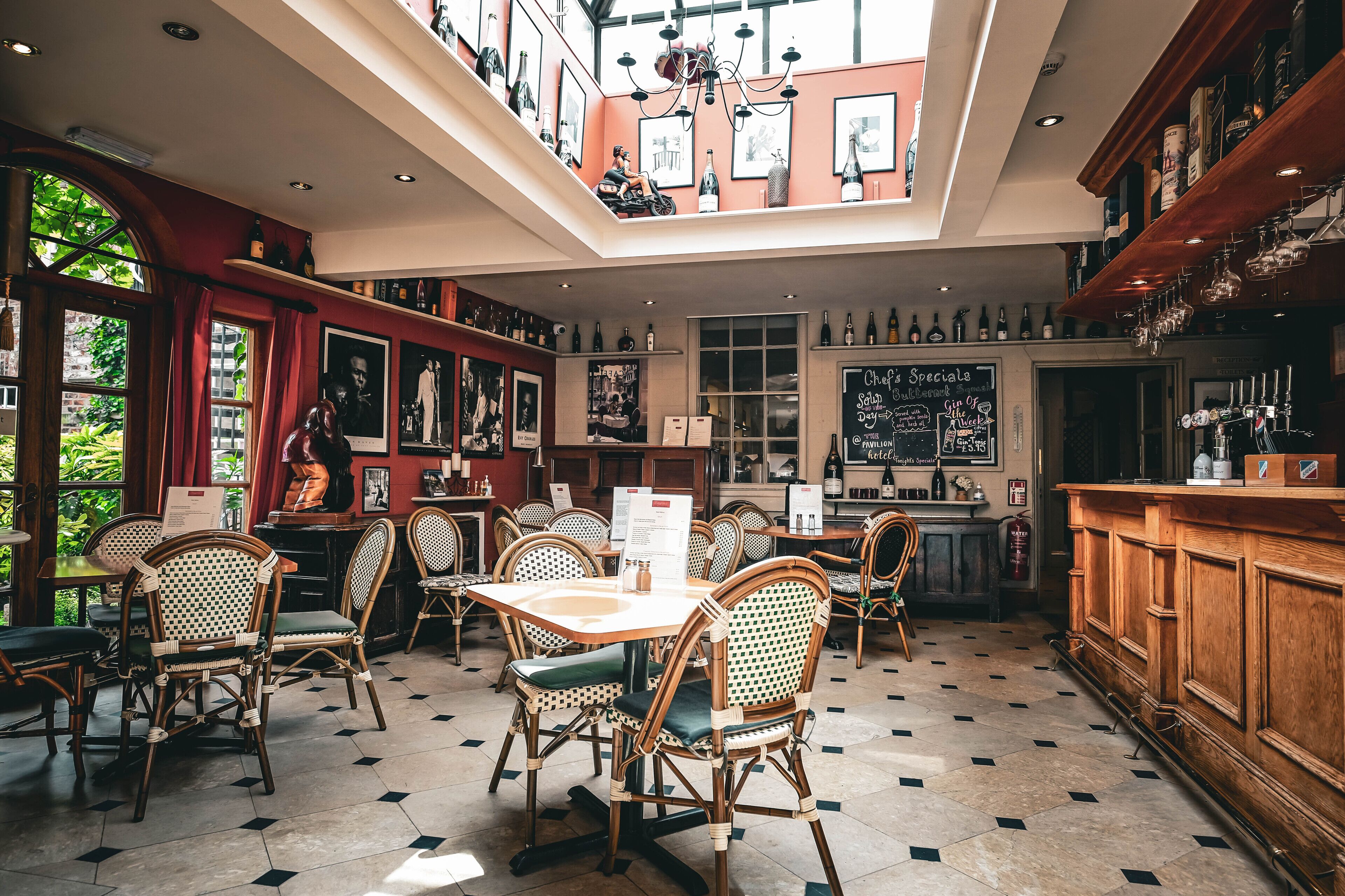A restaurant with a high ceiling, wooden chairs, a bar area, and a menu board.