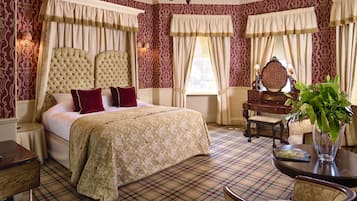 A bedroom with a large bed, a wooden nightstand, a dresser, a chair, and a table with a vase of flowers.