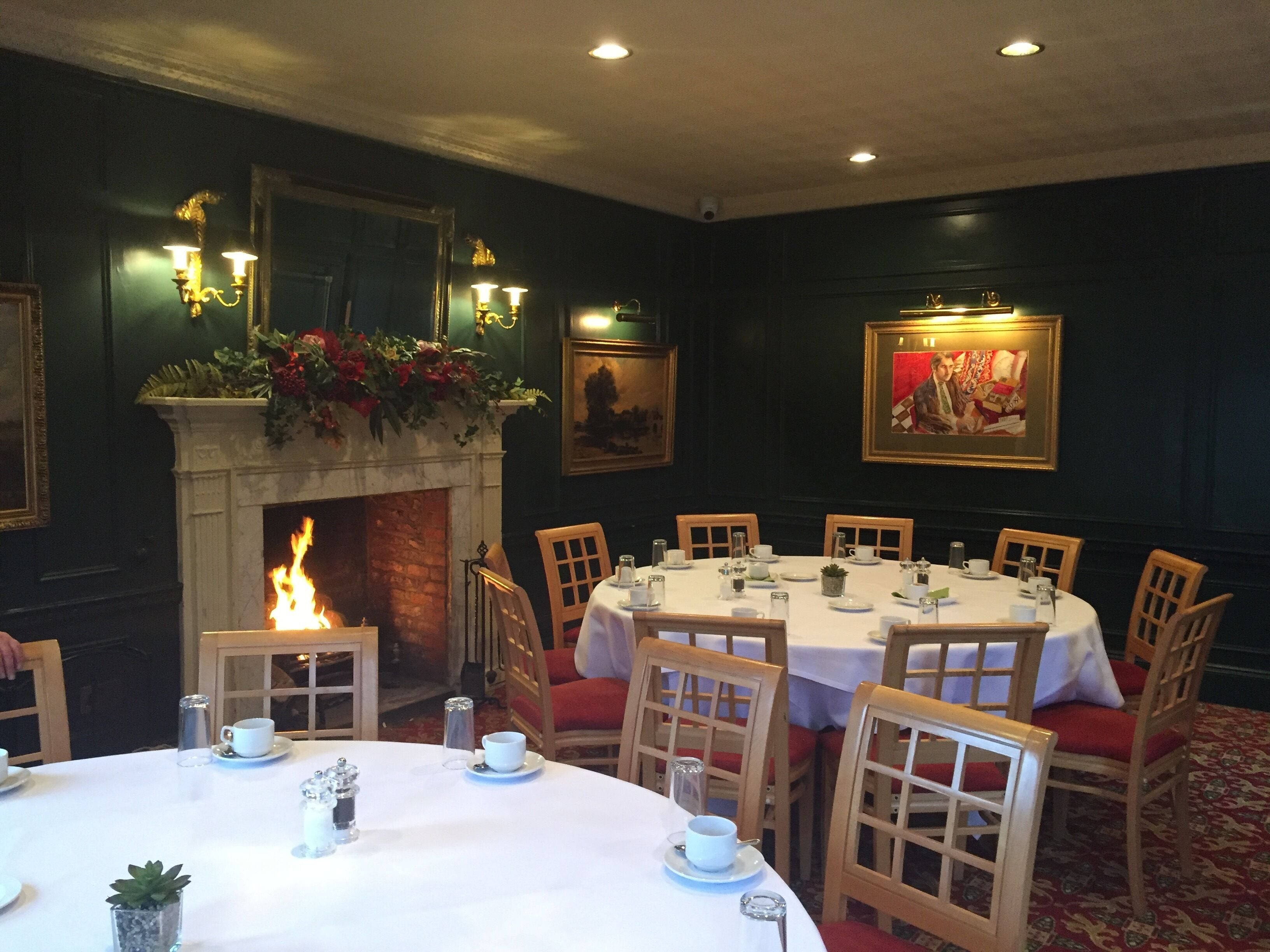A dining room with round tables, chairs, a fireplace, and wall-mounted lighting.