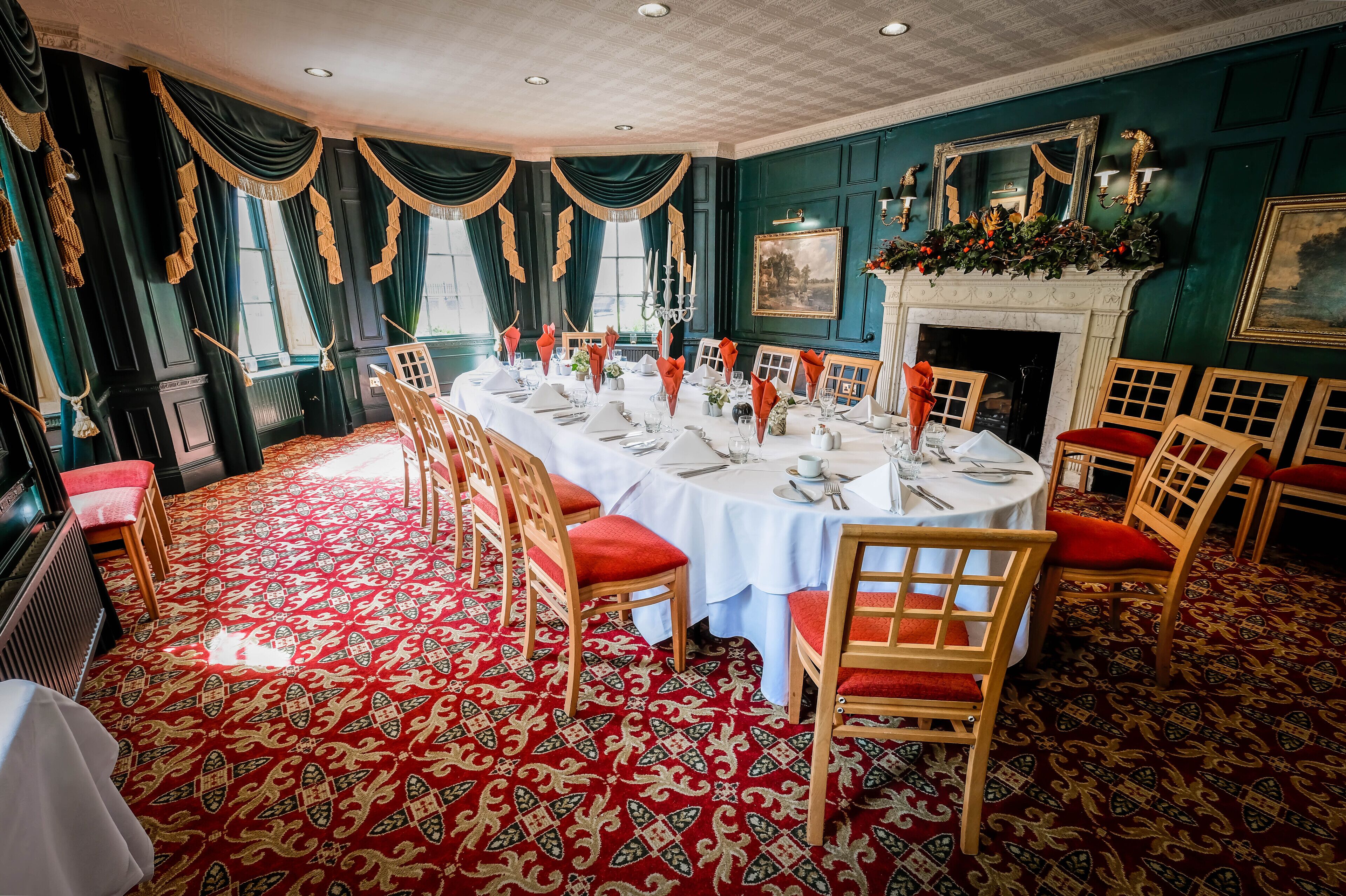A formal dining room with a long table set for a meal, surrounded by wooden chairs with red cushions.