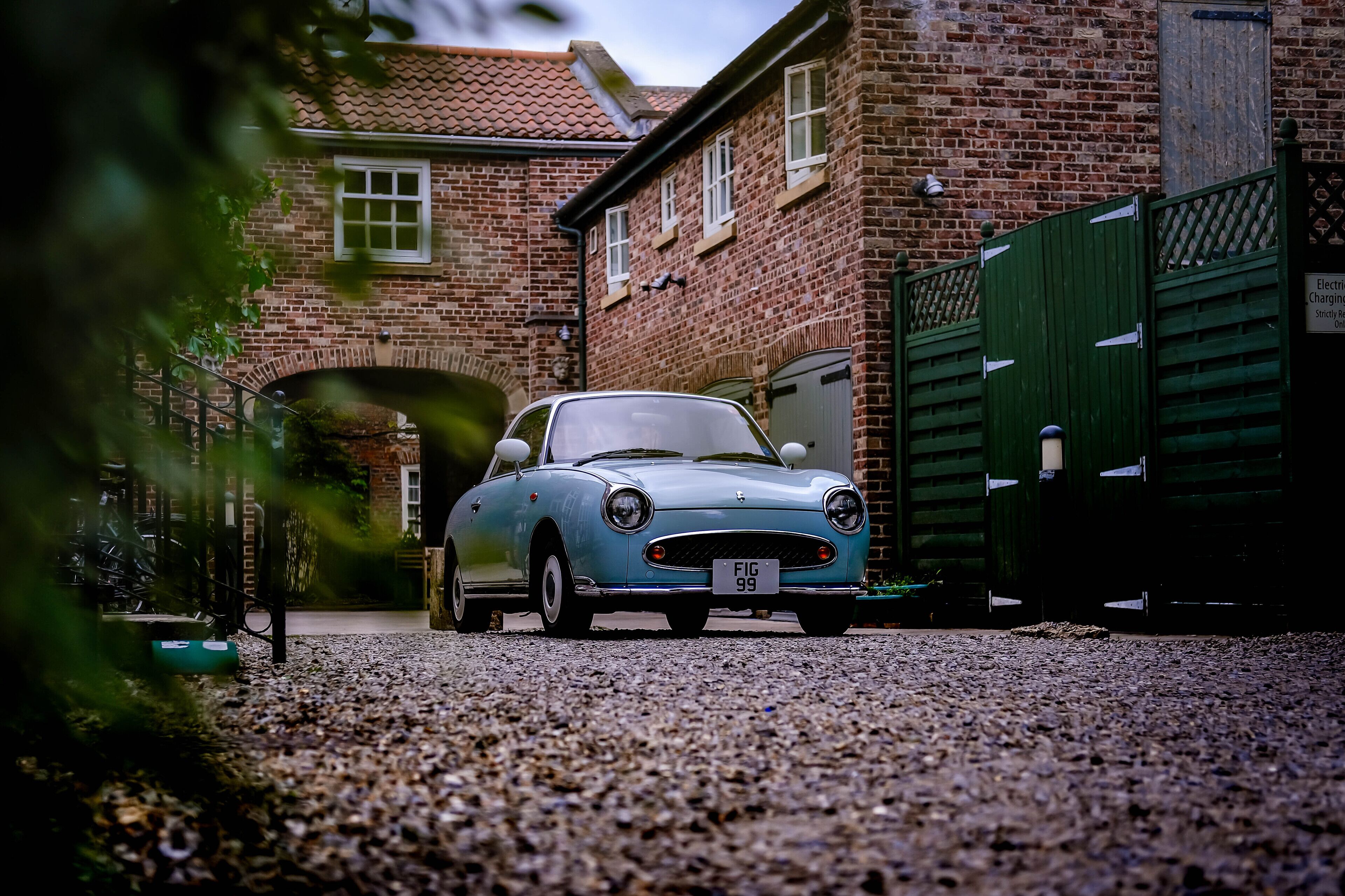 A vintage car parked in front of a brick building with a green gate.