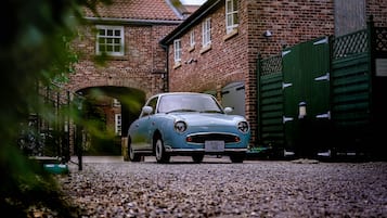 A vintage car parked in front of a brick building with a green gate.