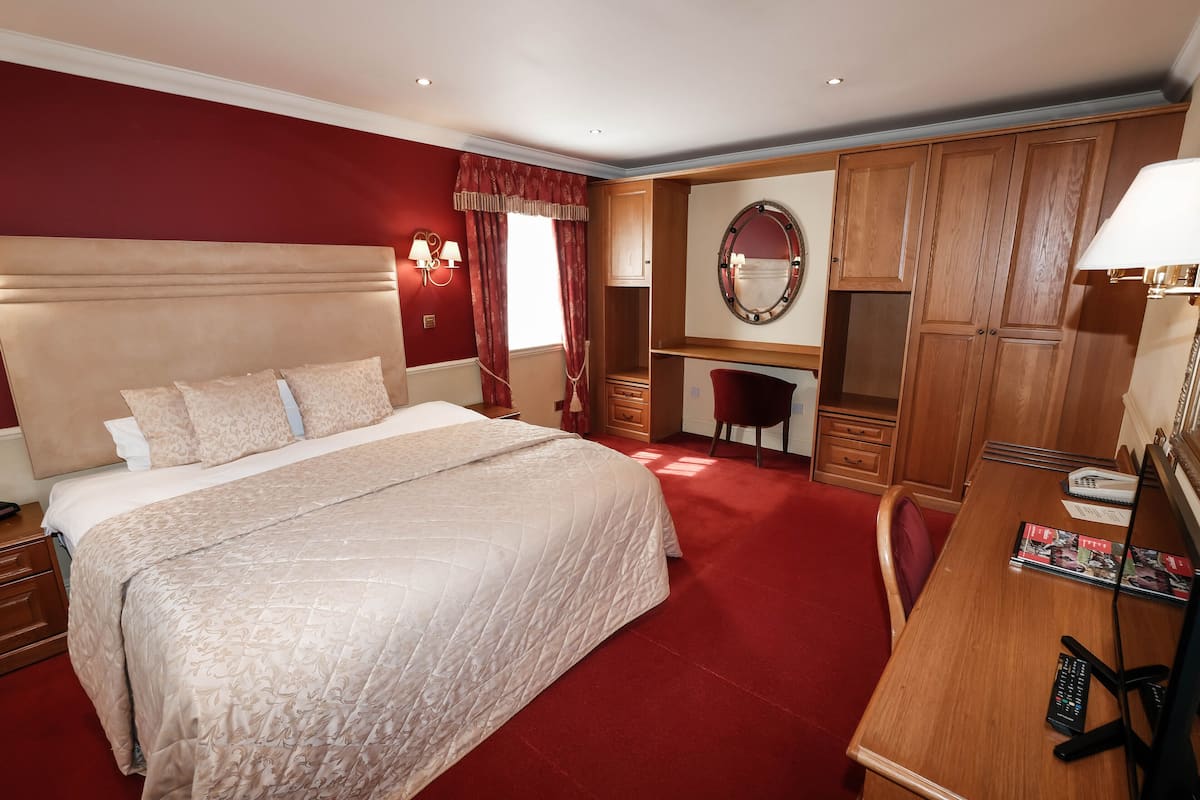 Une chambre d’hôtel avec un grand lit, un bureau avec un ordinateur, un miroir et des armoires en bois.