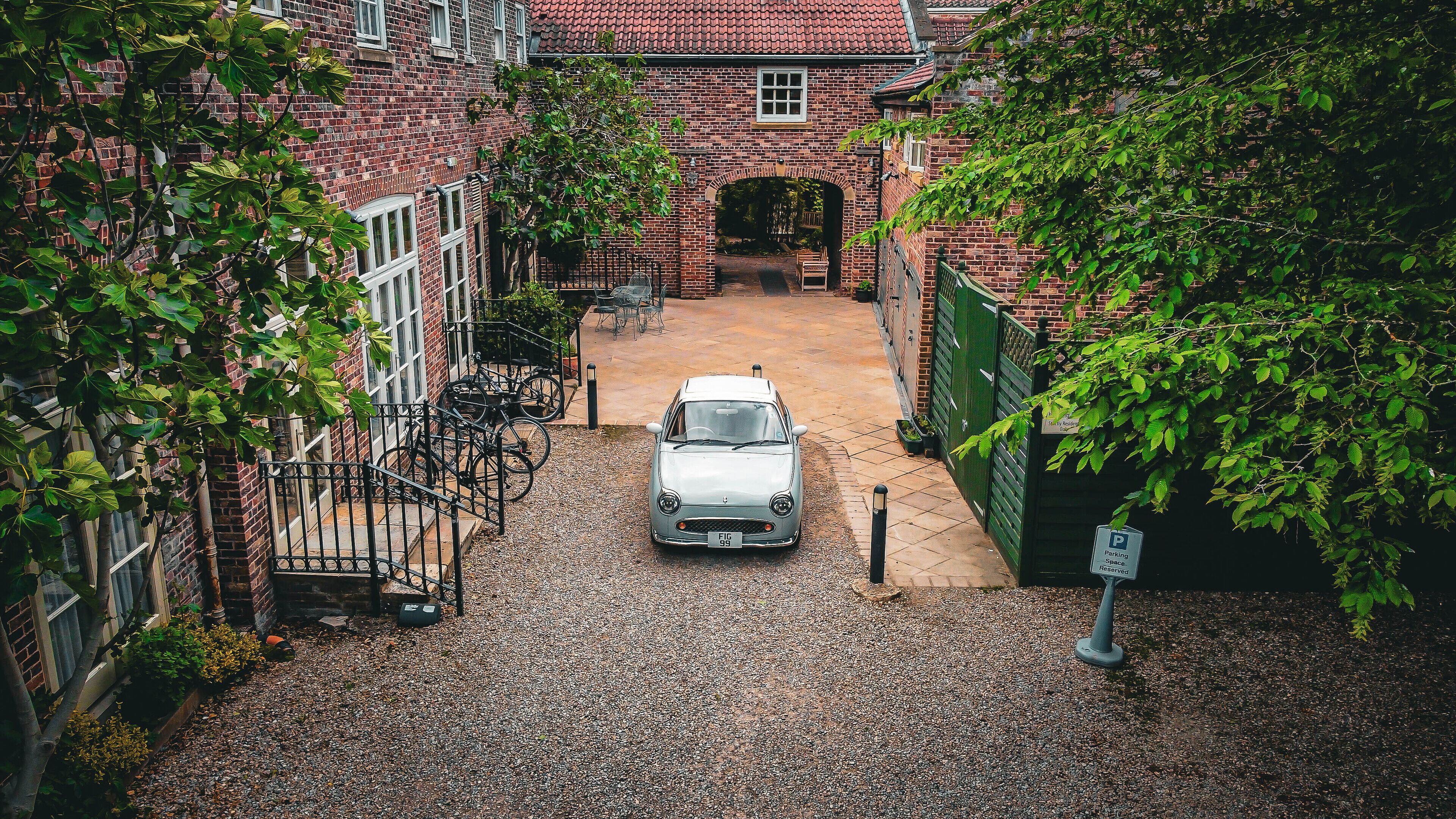 A narrow alleyway with a parked car, brick buildings, and a green gate.