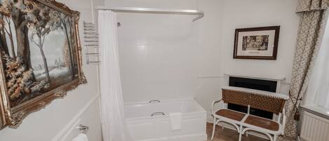 A bathroom with a bathtub, a white bench, a framed picture, and a radiator.