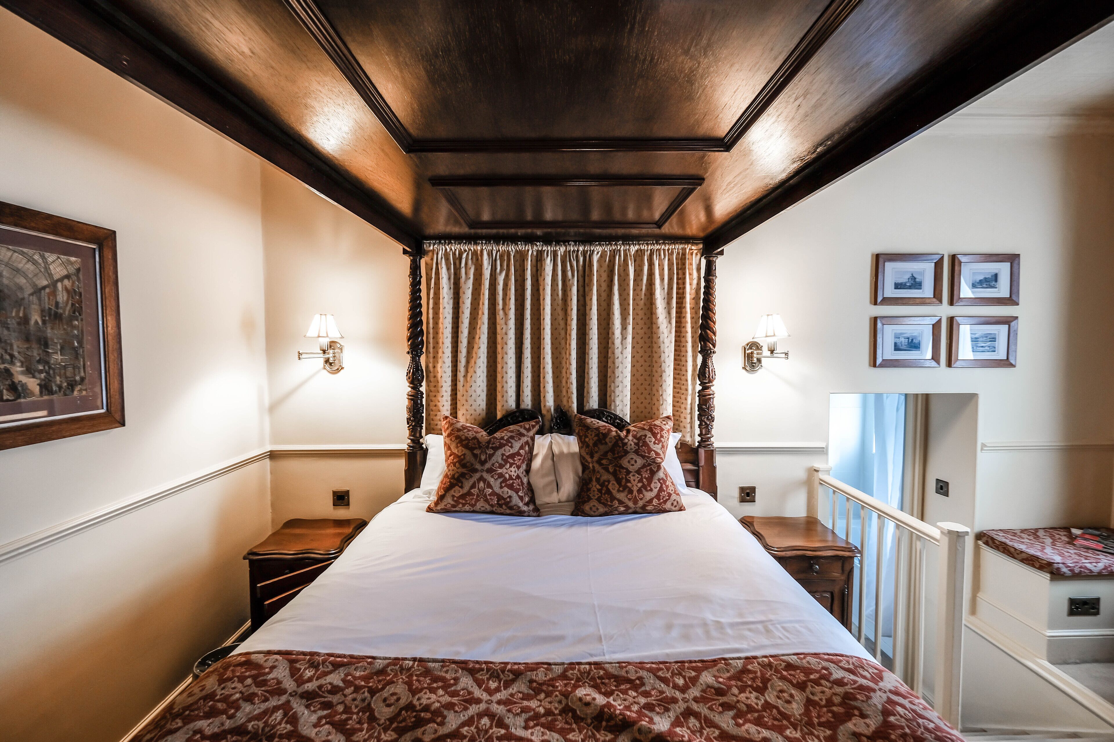 A hotel room with a large bed, two bedside tables, a headboard with curtains, wall-mounted lamps, and framed pictures.
