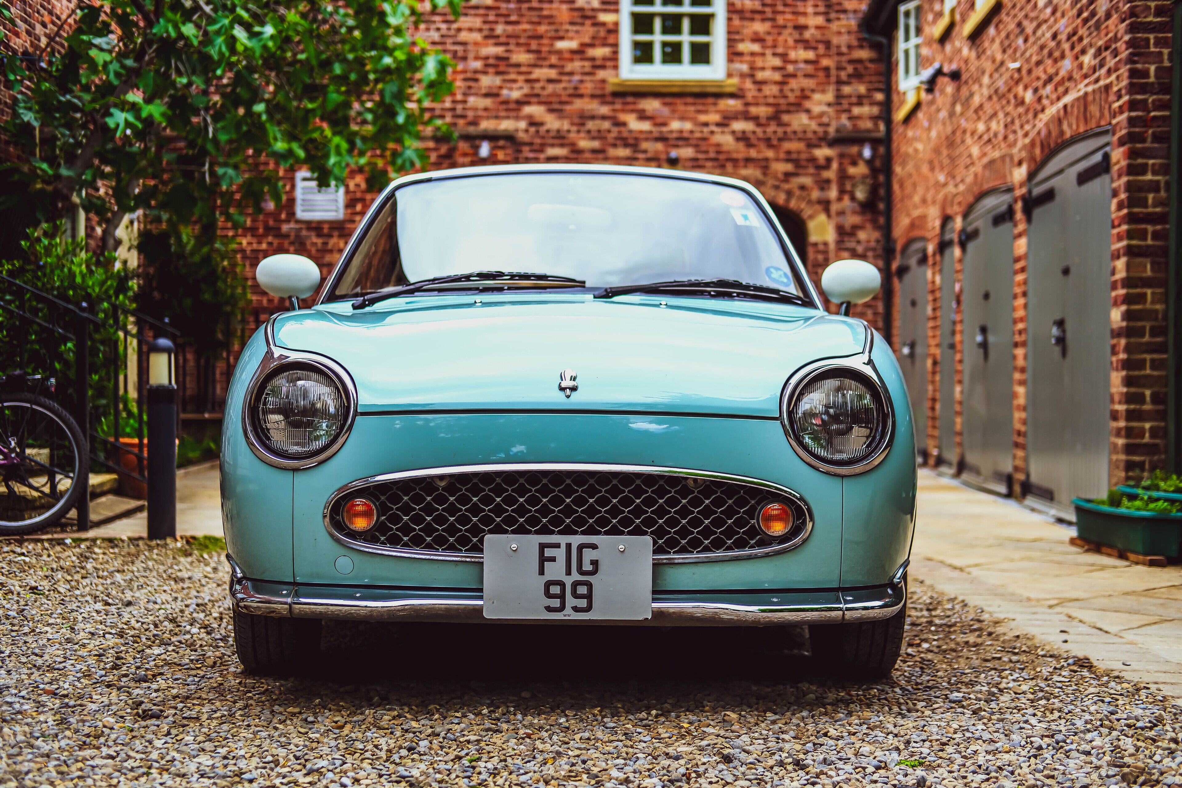 A vintage car parked in front of a brick building with a gravel driveway.
