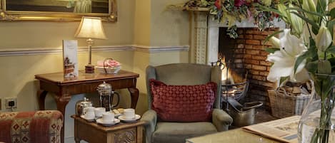 A cozy room with a fireplace, a table with tea set, a chair with a red cushion, and a vase with flowers.