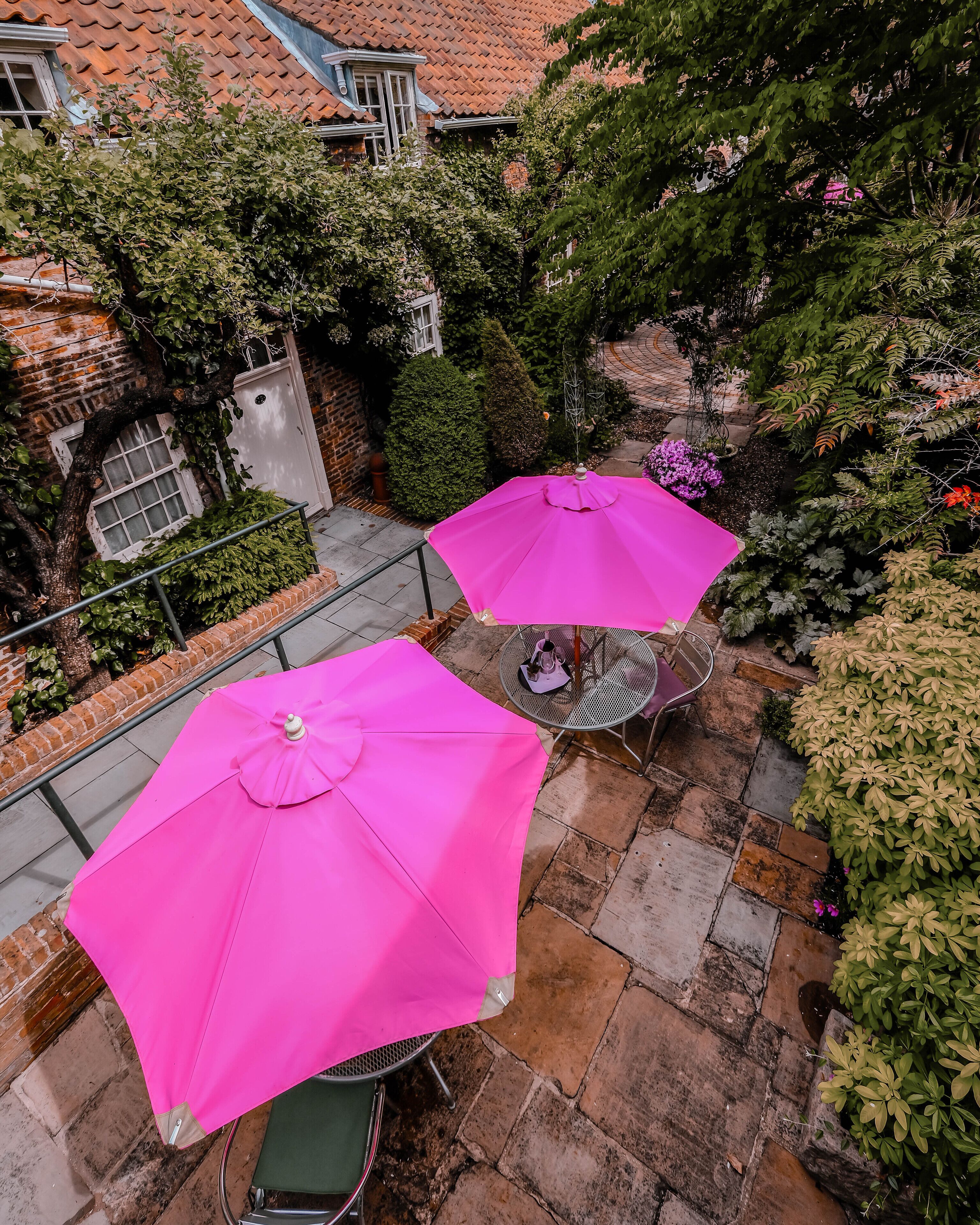 A courtyard with two pink umbrellas, a metal table, and chairs.