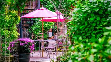 A garden patio with tables and chairs, surrounded by lush greenery and a brick wall.